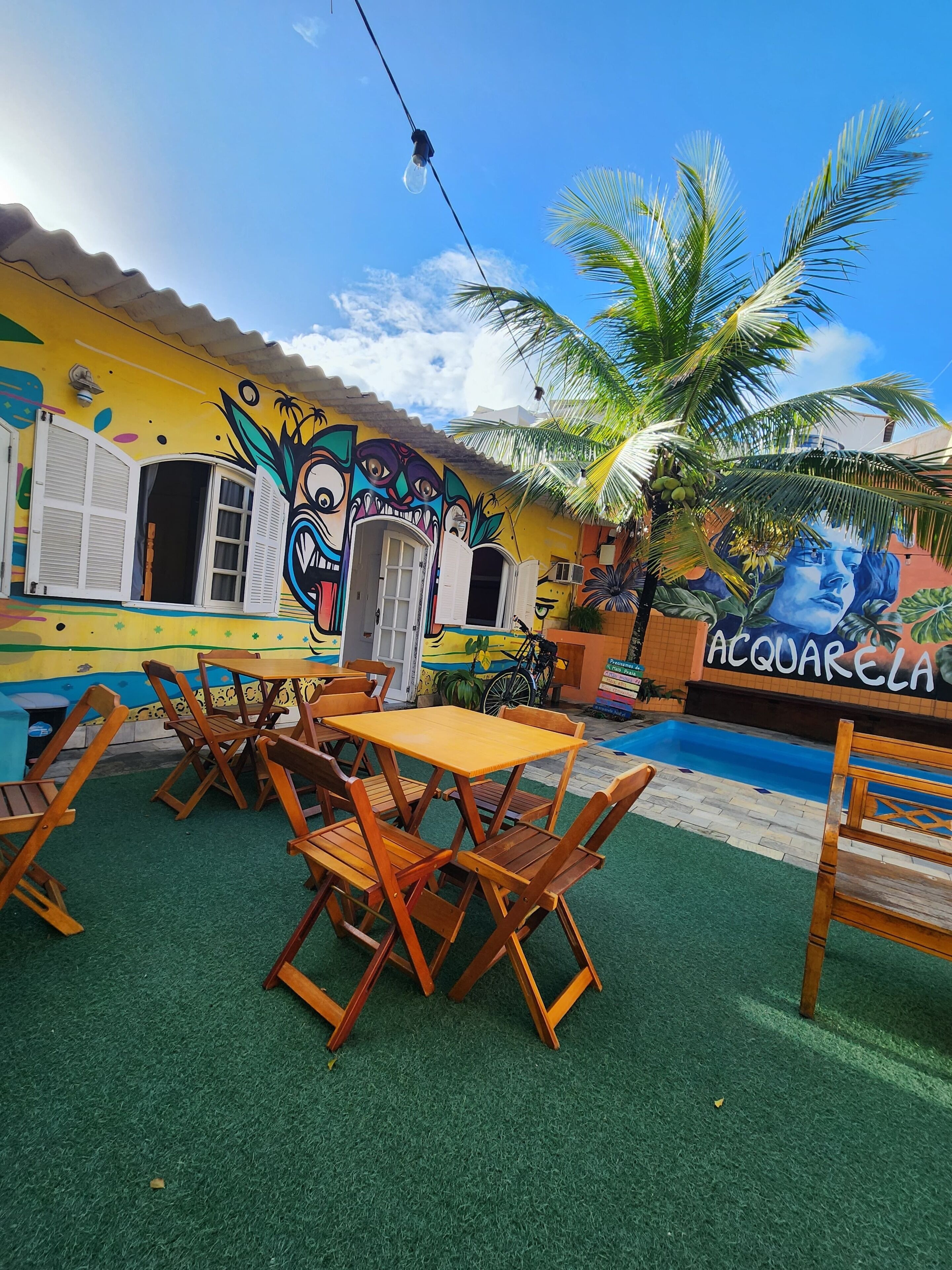 A vibrant outdoor seating area with wooden furniture, a mural, and a pool.