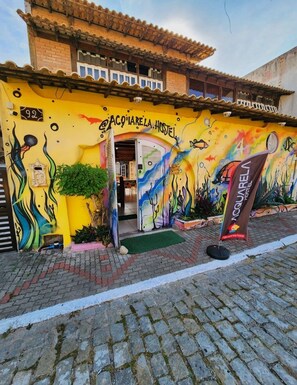 A hostel with a colorful mural, a sign reading 'ACQUAIRELA HOSTEL,' and a brick exterior.