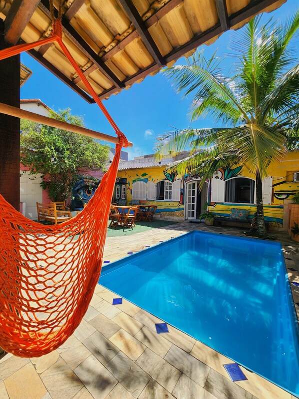A pool area with a hammock, a tiled floor, and a building with colorful murals.