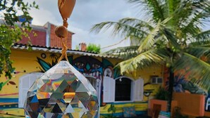 A hanging crystal ornament, outdoor seating with wooden chairs, a palm tree, and a colorful building with murals.