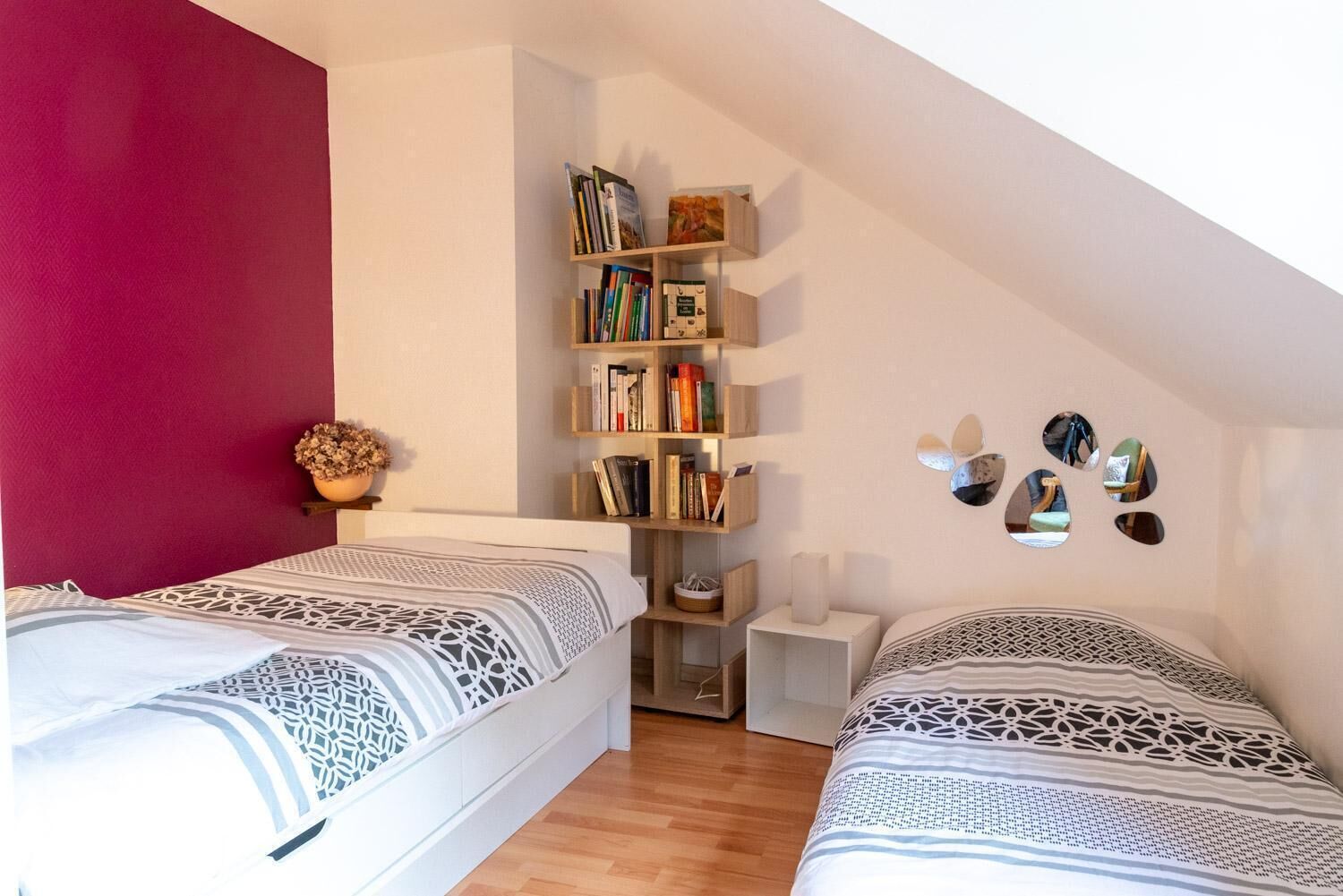 Ein Schlafzimmer mit zwei Betten, einem Bücherregal, einem Spiegel und einer Zimmerpflanze.
