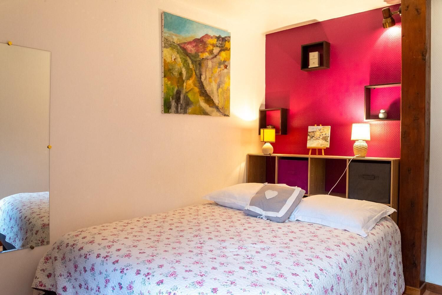 Un dormitorio con cama, un cuadro, una pared de acento roja y lámparas de noche.