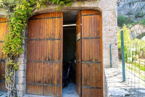 A rustic stone building with wooden double doors, a bicycle inside, and a stone wall with climbing plants. - Gîte Dardenne - LA MALENE (LA MALENE)