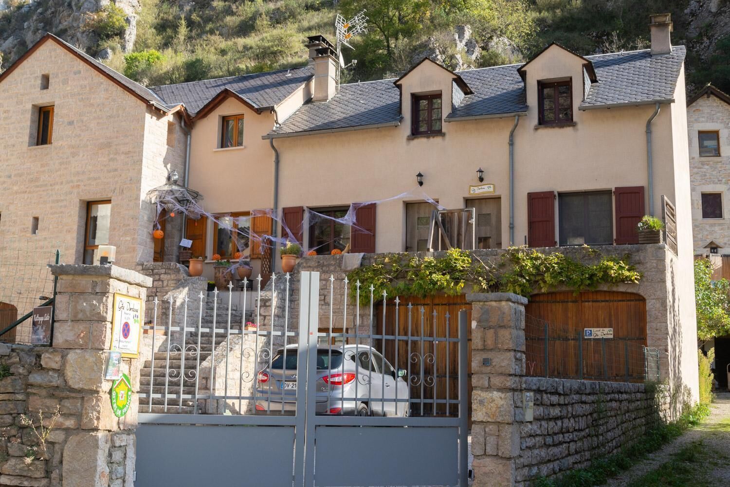Un bâtiment en pierre avec une entrée fermée par un portail, une voiture garée et un panneau indiquant une zone de stationnement.