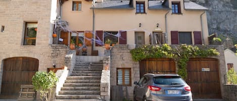 A stone building with a car parked in front, a staircase leading to the entrance, and a view of the surrounding landscape.