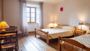 Quarto com duas camas de madeira, uma cadeira de madeira, uma mesa pequena e uma janela com cortinas.