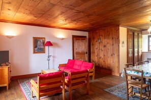 A wooden-paneled room with a red sofa, a small table, a TV, and a dining area with a table and chairs. - Gîtes de France in Fontanes (FONTANES)