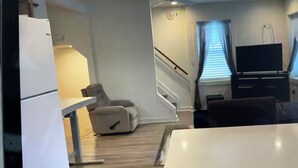 Ein kompakter Wohnraum mit Küchenzeile, einer Couch, einem Fernseher und einer Treppe.