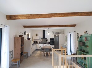 Eine geräumige Küche mit Holzbalken, einem Essbereich mit Stühlen und einem grünen Bücherregal.