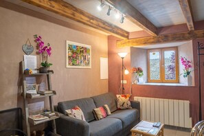 Ein gemütliches Wohnzimmer mit grauem Sofa, Holzboden und einem Fenster mit Ausblick, sowie einer Stehlampe.