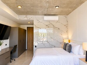 A modern bedroom with a marble wall, a bed with white bedding, a desk with a chair, and a TV mounted on the wall. - Modern Studio in Art Haus San Benito in the City's Most Exclusive Area (San Salvador)