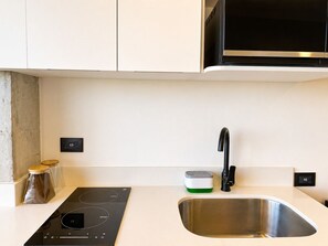 Una cocina con placa de inducción integrada, un lavamanos de acero inoxidable y un microondas sobre la encimera.