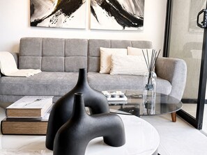 Una sala de estar moderna con un sofá gris, arte abstracto, una mesa de centro de vidrio y un florero negro.