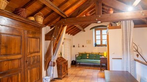 A rustic room with wooden beams, a green sofa, a wooden table, and a large wooden cabinet. - Gîtes de France 3 épis 2/3 persons Puychauzier (SAINT-JULIEN-D'ARPAON)
