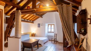 A rustic room with a bed, a wooden table, a chair, a window, and a shelf with items. - Gîtes de France 3 épis 2/3 persons Puychauzier (SAINT-JULIEN-D'ARPAON)
