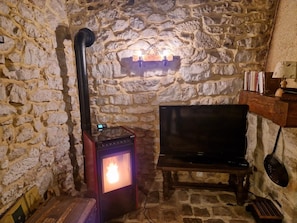 Ein Zimmer mit Stehwänden, einem Kaminofen, einem Fernseher und einem Bücherregal.