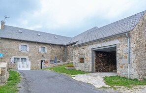 A stone building with a garage, a paved driveway, and a small garden area. - Gîte de Montchamp - ARZENC D'APCHER (ARZENC D'APCHER)