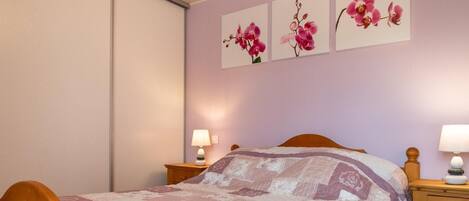 Un dormitorio con una cama, dos mesitas de noche y tres cuadros de flores colgados en la pared.