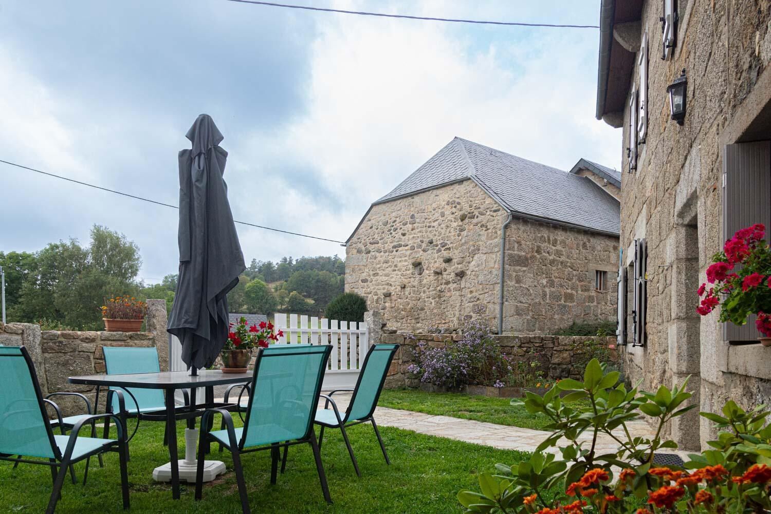 A stone building with a sloped roof, a patio with chairs and a table, and a white picket fence.