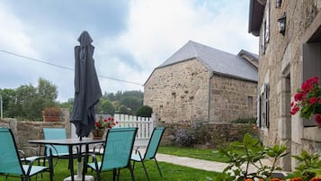 A stone building with a sloped roof, a patio with chairs and a table, and a white picket fence.