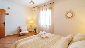 Ein Hotelzimmer mit einem Bett, einem Sessel, einer Lampe, einer Topfpflanze und einer Wanddekoration in Sonnenform.