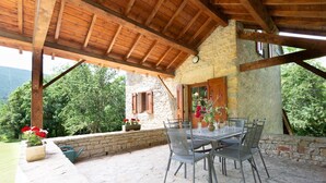 Un patio exterior con suelo de piedra, techo de madera y una mesa con sillas.