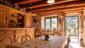A rustic kitchen with wooden cabinets, a dining table, and a stone wall. - L'Echappée de la Lozère - LES LAUBIES (LES LAUBIES)