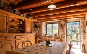 A rustic kitchen with wooden cabinets, a dining table, and a stone wall. - L'Echappée de la Lozère - LES LAUBIES (LES LAUBIES)