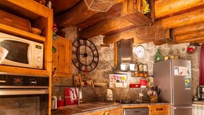 A rustic kitchen with wooden cabinets, a microwave, a clock, a stove, and a refrigerator. - L'Echappée de la Lozère - LES LAUBIES (LES LAUBIES)