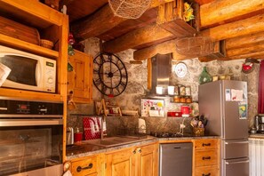 A rustic kitchen with wooden cabinets, a microwave, a clock, a stove, and a refrigerator. - L'Echappée de la Lozère - LES LAUBIES (LES LAUBIES)