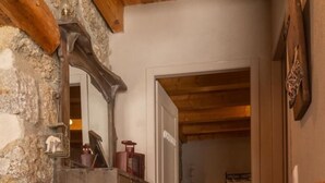 A hallway with a stone wall, a wooden ceiling, a mirror, a potted plant, and a door leading to another room. - L'Echappée de la Lozère - LES LAUBIES (LES LAUBIES)