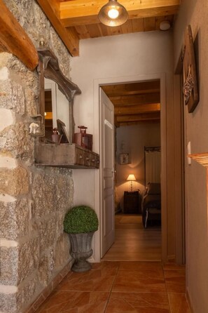 A hallway with a stone wall, a wooden ceiling, a mirror, a potted plant, and a door leading to another room. - L'Echappée de la Lozère - LES LAUBIES (LES LAUBIES)