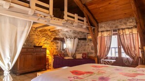 A rustic bedroom with a loft bed, stone walls, wooden beams, and a bed with a floral bedspread. - L'Echappée de la Lozère - LES LAUBIES (LES LAUBIES)