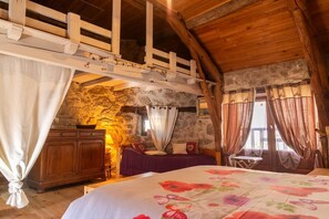 A rustic bedroom with a loft bed, stone walls, wooden beams, and a bed with a floral bedspread. - L'Echappée de la Lozère - LES LAUBIES (LES LAUBIES)