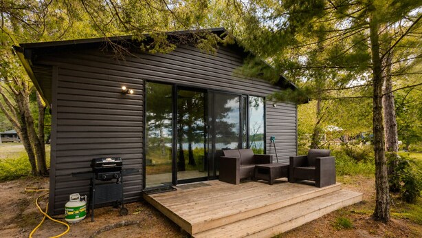 A modern cabin with a deck, outdoor grill, and a gas canister. - Deluxe 3-Bedroom Cottage #12 (Nobel)