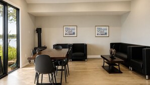A modern living room with a dining area, black leather sofas, a wooden dining table, and two framed pictures on the wall. - Deluxe 3-Bedroom Cottage #12 (Nobel)