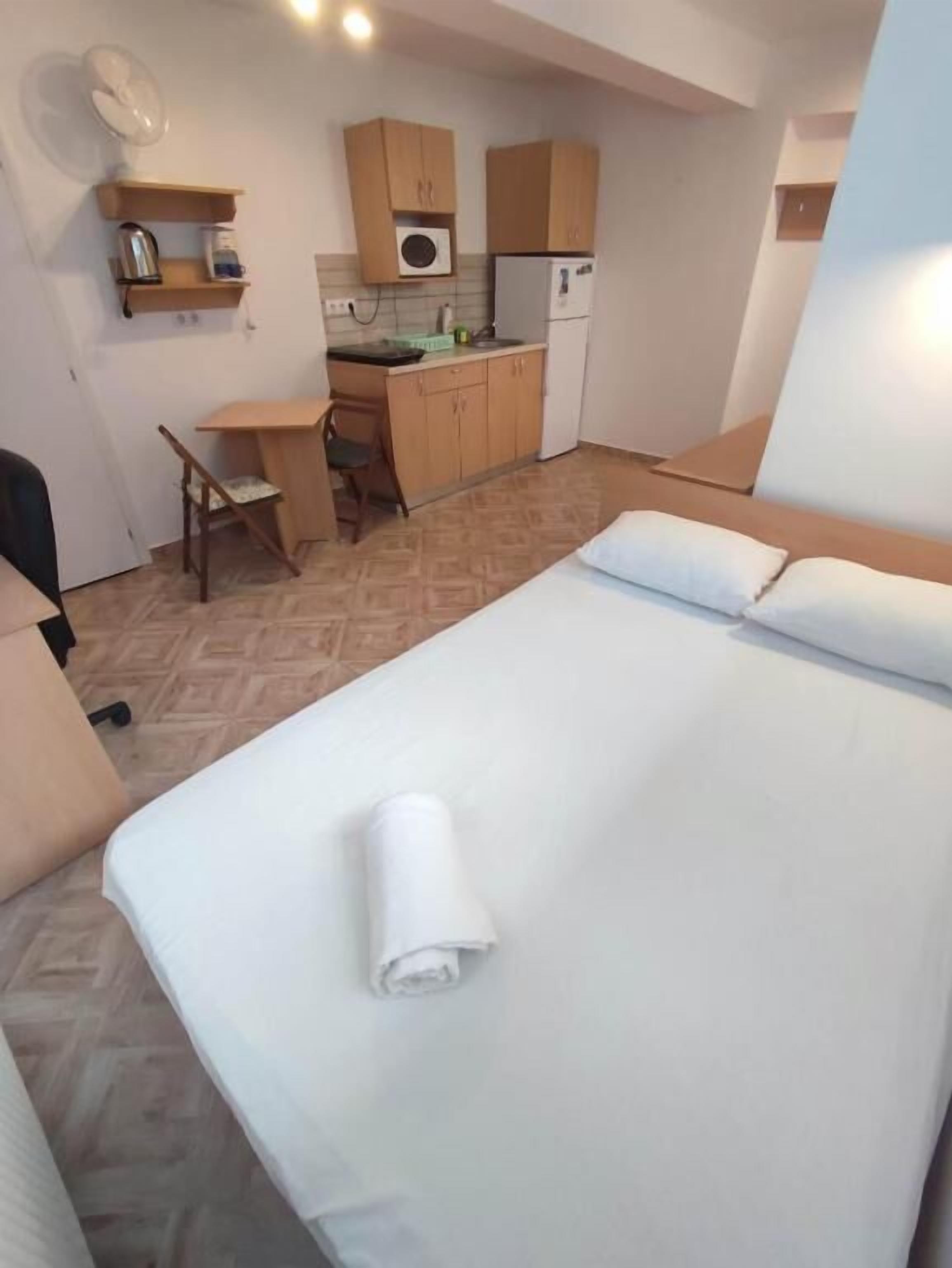 Ein kompaktes Hotelzimmer mit Bett, Schreibtisch, Stuhl, einer Küchenzeile und einer kleinen Sitzecke.