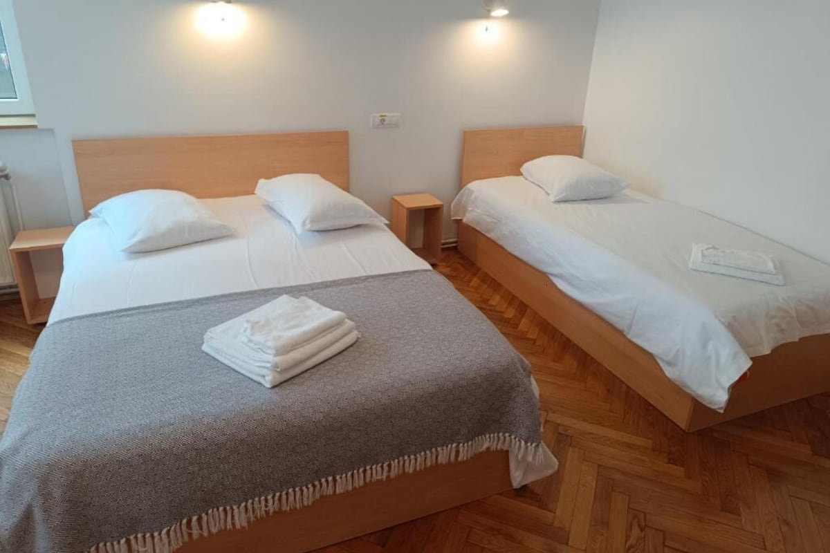 A hotel room with two single beds, wooden headboards, bedside tables, and wall-mounted lights.