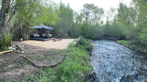 A campsite with a covered seating area, a river, and surrounding trees. - Charming cabin tent campground in peaceful Frenchtown for your getaway (Frenchtown)
