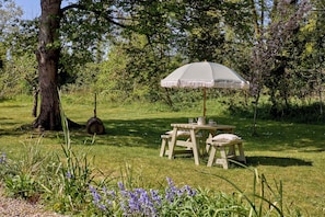 A picnic setup with a table and bench, surrounded by greenery and trees. - The Little Duke | Cosy Hideaway near Southwold (Halesworth)
