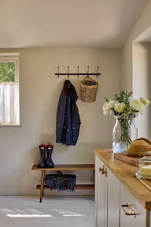 A room with a coat rack, a basket, a bench with boots and a bag, a vase with flowers, and a wooden table with a bread loaf. - The Little Duke | Cosy Hideaway near Southwold (Halesworth)