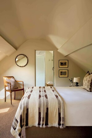 Ein Schlafzimmer mit einem Bett, einem Sessel, einem Spiegel und zwei gerahmten Bildern an der Wand.