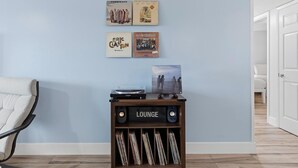 A lounge area with a record player, a wall-mounted shelf with vinyl records, and a door leading to another room. - Sea Coast Condominium 517 (New Smyrna Beach)