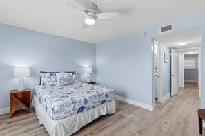 Ein Schlafzimmer mit einem Bett, Nachttischen, einem Deckenventilator und einem Flur, der zu einer Tür führt.