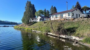 Une propriété située au bord d’un lac, avec un bâtiment blanc, une jetée et un ciel bleu dégagé.