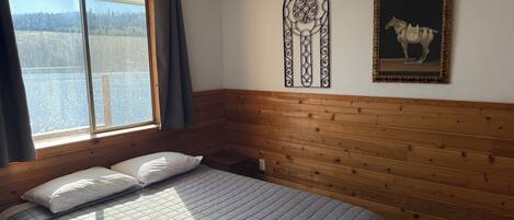 A room with a bed, a window with curtains, a wall-mounted decorative piece, and a framed picture.