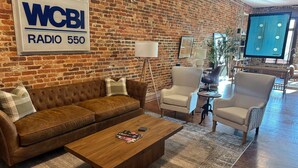 A cozy living area with a leather sofa, a wooden coffee table, and two armchairs. A brick wall with a radio sign is visible. - Historic Media Loft in Downtown Columbus - Newly Renovated - Walk Everywhere (Columbus)