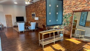 A living room with a brick wall, wooden flooring, a ceiling fan, a TV, and a large mirror. - Historic Media Loft in Downtown Columbus - Newly Renovated - Walk Everywhere (Columbus)