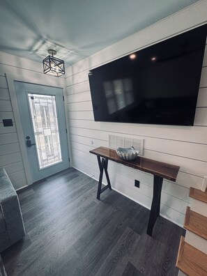 Un intérieur moderne avec un téléviseur à écran plat fixé au mur, un banc en bois et une porte ornée d’un panneau de verre décoratif.