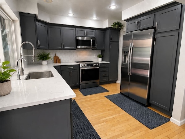 Une cuisine moderne avec des meubles de couleur sombre, des appareils en acier inoxydable, un plan de travail blanc et un plancher en bois.